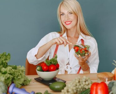 Blonde woman enjoying a fresh salad surrounded by vegetables, promoting healthy eating.