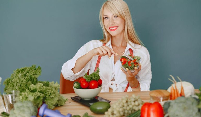 Blonde woman enjoying a fresh salad surrounded by vegetables, promoting healthy eating.
