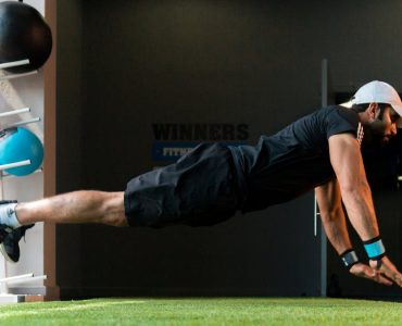 Middle Eastern man doing explosive pushups on gym turf.