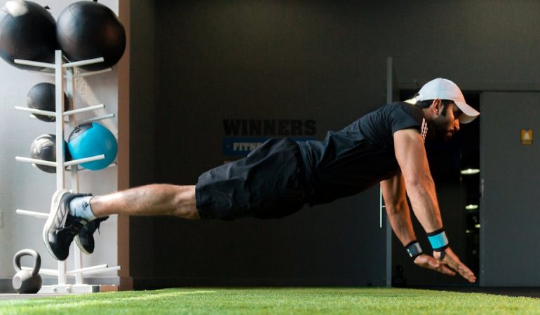 Middle Eastern man doing explosive pushups on gym turf.